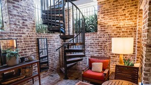 A cozy room with a brick wall, a spiral staircase, a red chair, a wooden table, and a lamp. - Luxurious Mansion Downtown Charleston (Charleston)