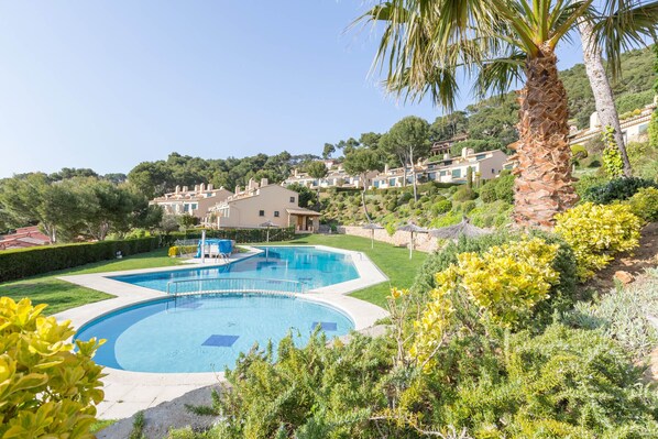 Une piscine entourée de verdure, avec une colline parsemée de maisons en arrière-plan.