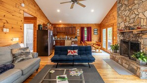 A cozy cabin interior with a living room, kitchen, and stone fireplace.
