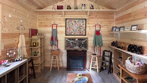 A cozy wooden interior with shelves displaying kitchen items, a fireplace, and a wall with framed pictures.