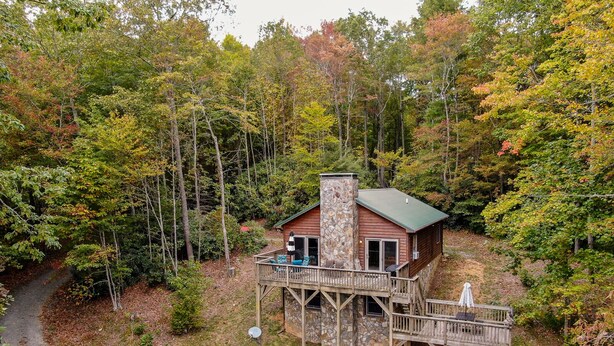 A cabin with a stone chimney, wooden deck, and a small porch.