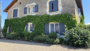 A two-story house with a stone facade, ivy-covered walls, and multiple windows with shutters.