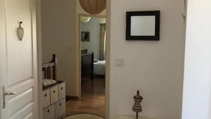 A hallway with a wooden floor, a white door, a small white table with a decorative item, and a framed mirror on the wall.