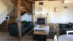 A cozy living room with a fireplace, wooden beams, and a staircase.