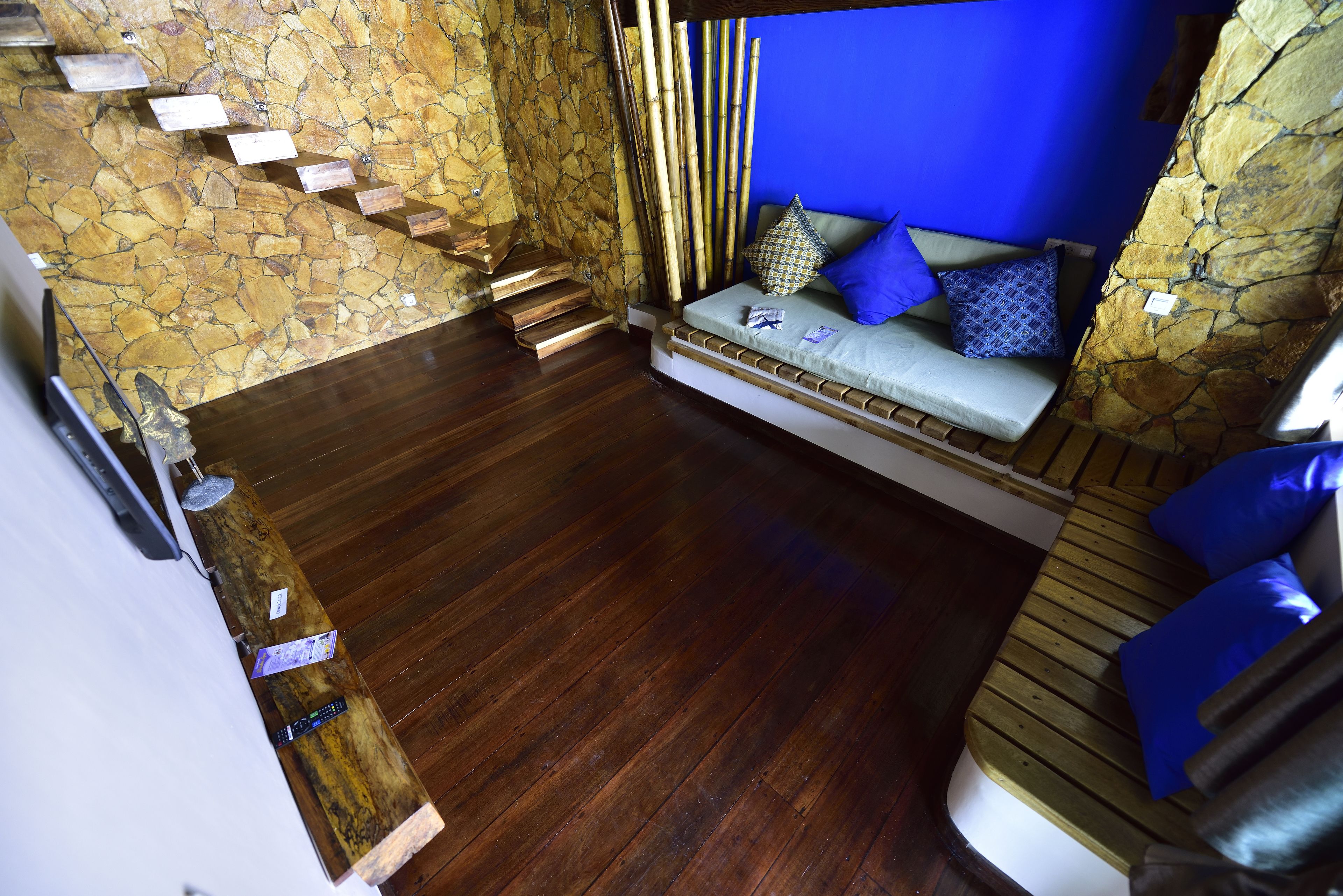 A room with a stone wall, a wooden floor, a built-in bench with cushions, and a staircase.