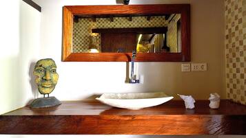 A bathroom with a wooden vanity, a sink with a vessel basin, a mirror, and a decorative head sculpture.