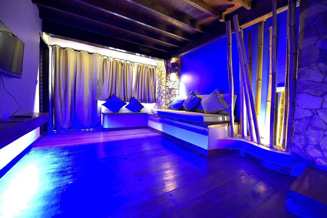 Una habitación con pared de piedra, techo de madera y una zona de estar con cojines.