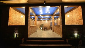 Un intérieur aux murs de briques, avec des poutres apparentes et des luminaires suspendus.