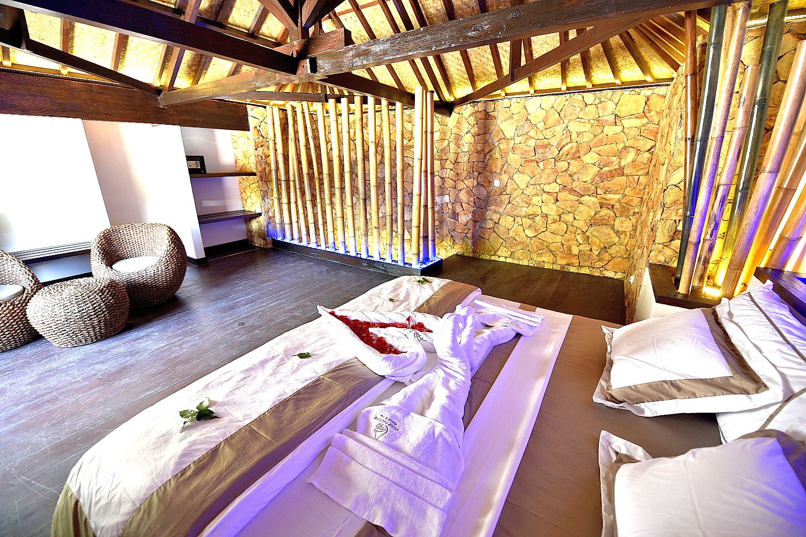A spa room with a stone wall, wooden beams, and a massage table with towels.