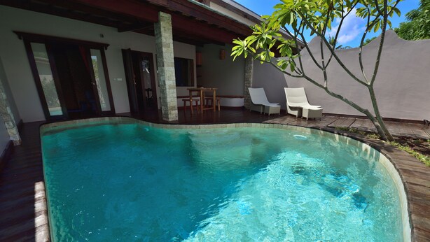 Une piscine avec une terrasse en bois, un patio couvert et quelques chaises longues.
