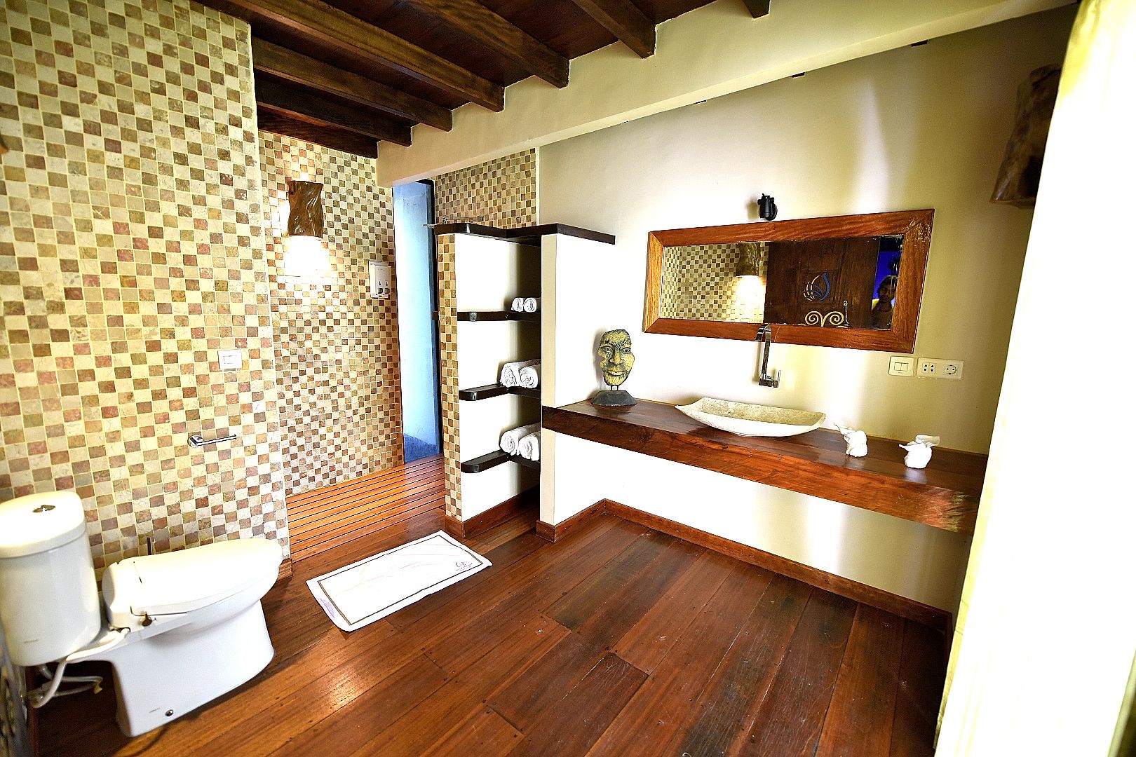 A bathroom with a tiled wall, wooden floor, a sink with a mirror, and a toilet.