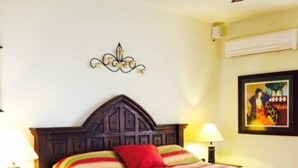 A bedroom with a wooden headboard, a colorful striped bedspread, two bedside lamps, and a ceiling fan.