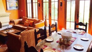 A dining area with a wooden table set for four, a sofa, and a painting on the wall.