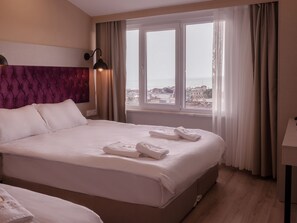 A hotel room with a large bed, a view of the city through a window, and a bedside lamp. - The Lola Hotel (Istanbul)
