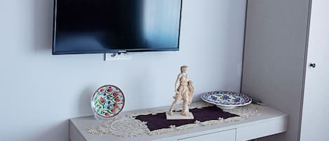 A flat-screen TV mounted on a wall above a white console table with decorative plates and a statue.