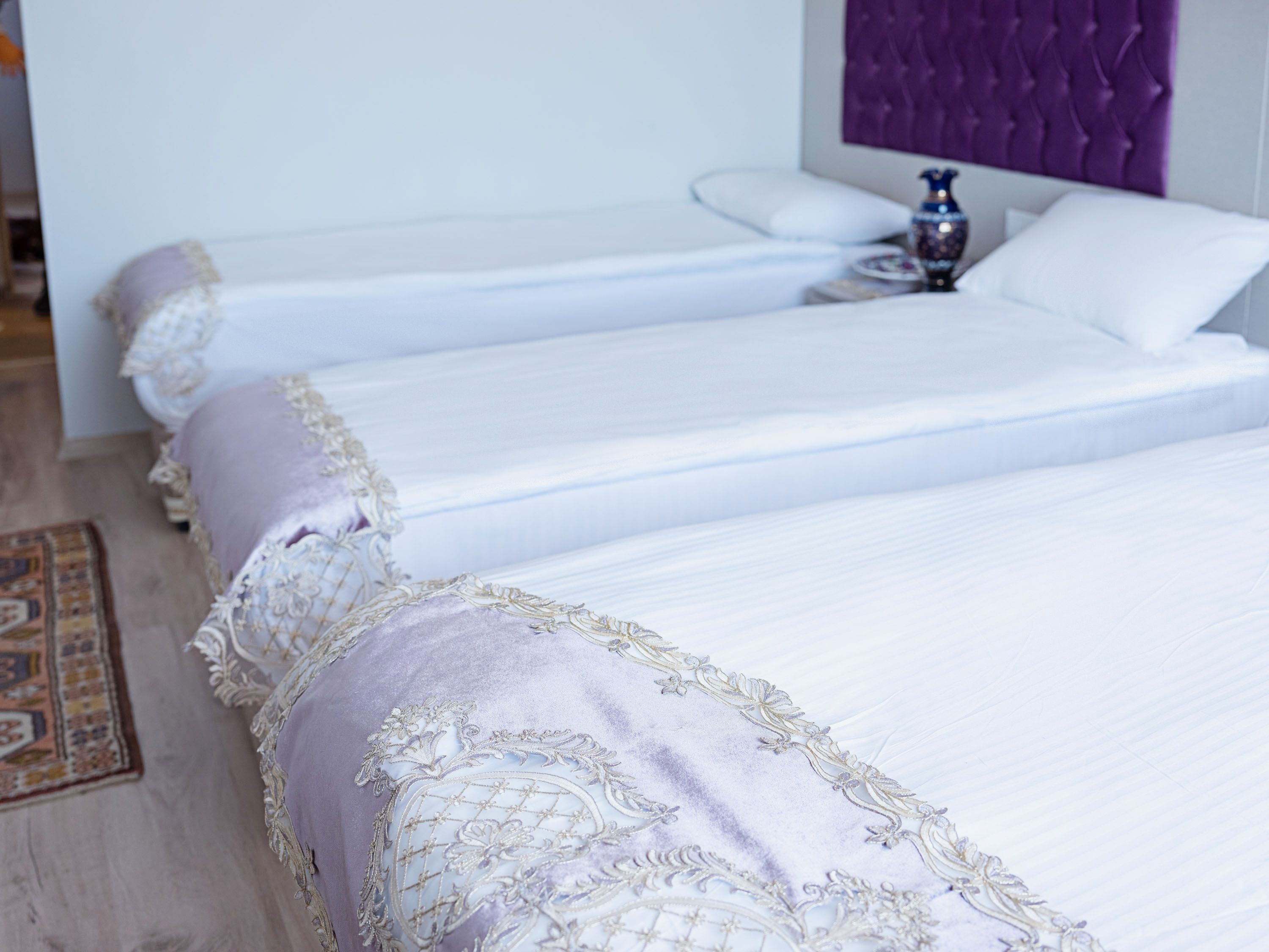 Habitación de hotel con dos camas, cada una con ropa blanca y almohadas decorativas moradas.