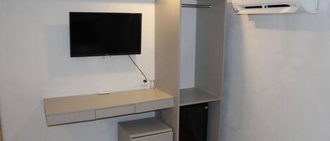 A compact room with a built-in TV, a mini fridge, and a wall-mounted air conditioner.