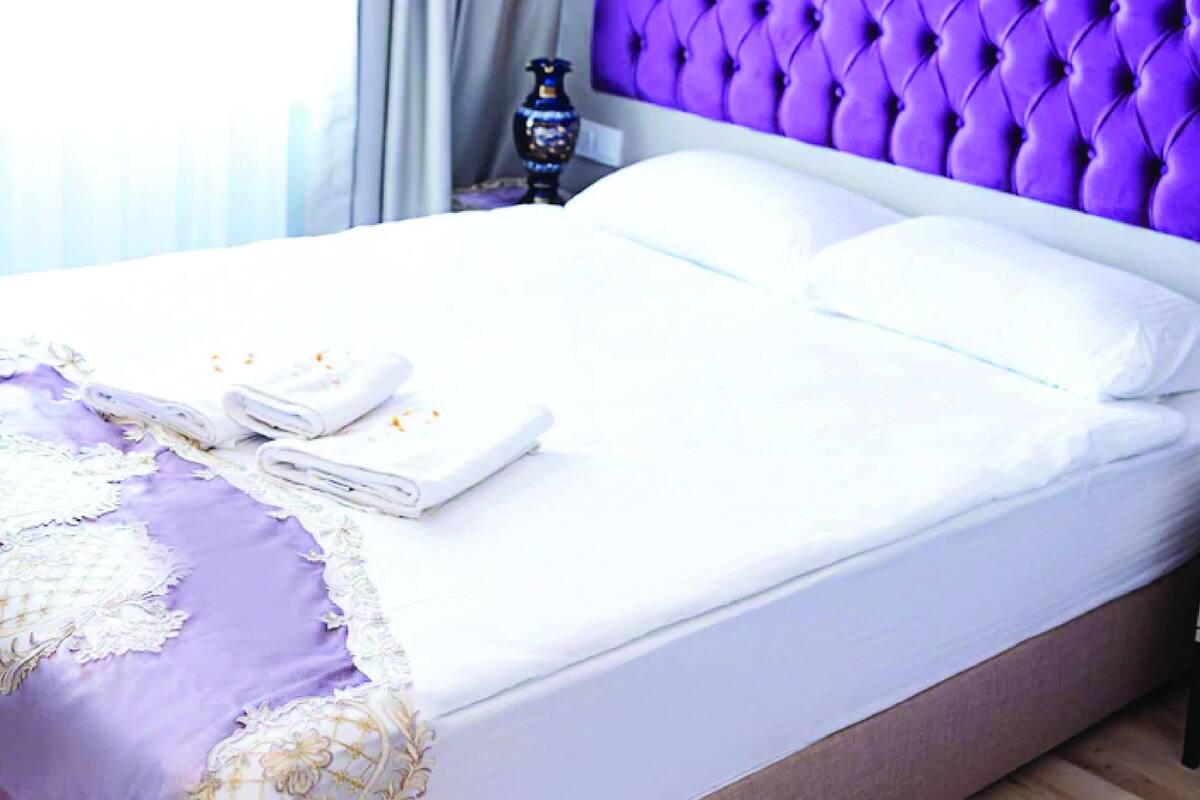 A neatly made bed with white linens and a purple headboard.