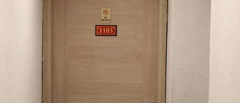 A wooden door with a "No Smoking" sign and a room number "1103" on a hotel wall.