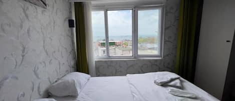 Een hotelkamer met een bed, een raam met uitzicht op gebouwen en behang met een patroon.