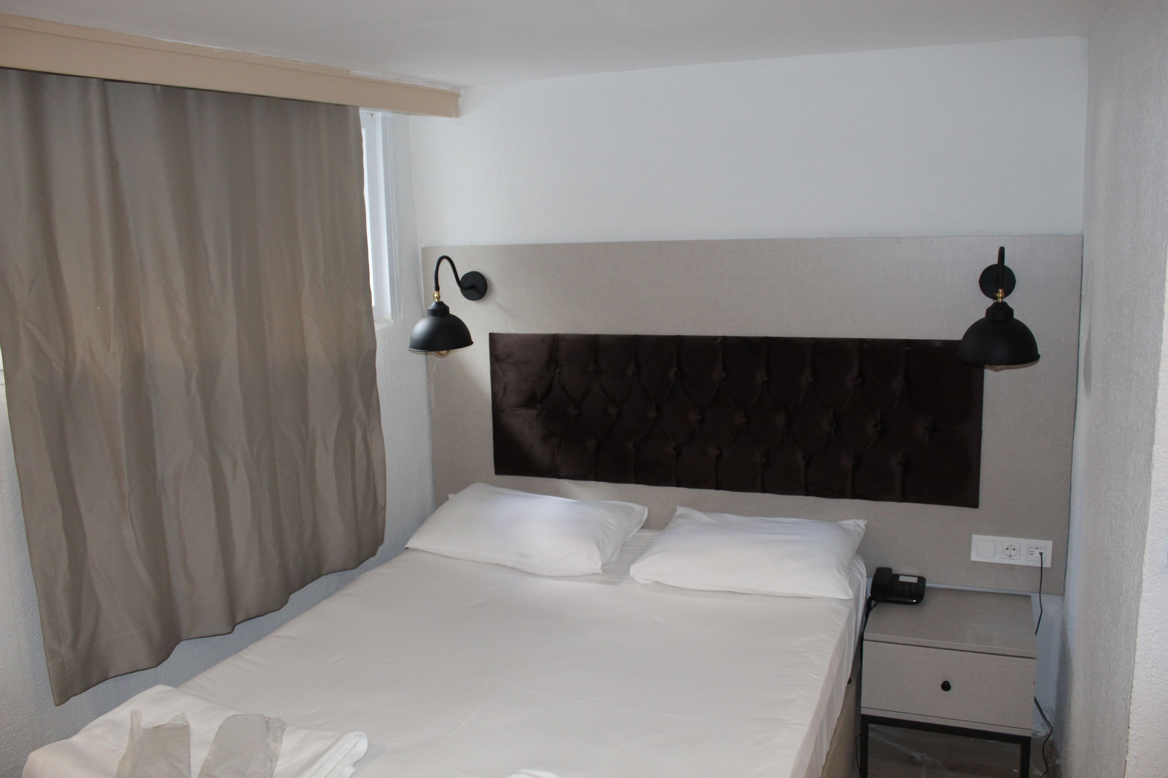 A hotel room with a large bed, two bedside lamps, a nightstand, and a window with curtains.