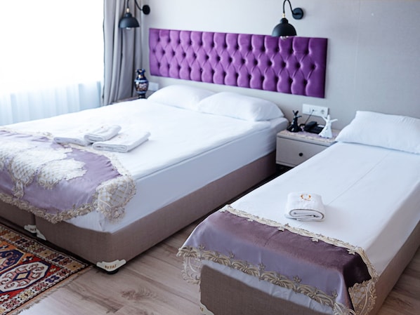 A hotel room with two beds, a purple headboard, white bedding, a nightstand, a lamp, and a decorative vase. - The Lola Hotel (Istanbul)