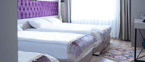 A hotel room with two beds, a purple headboard, a small table, and a patterned rug.