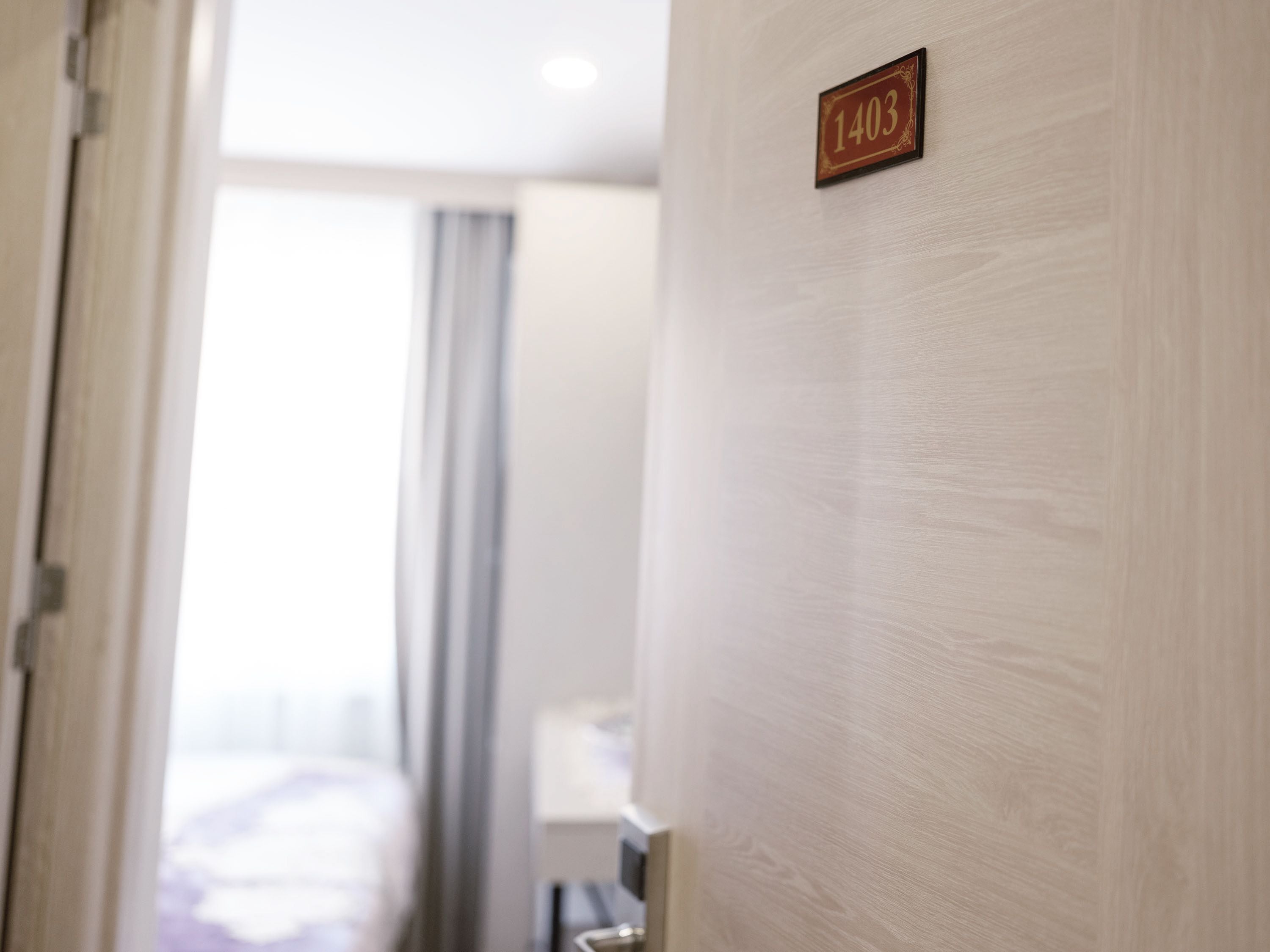 A hotel room with a wooden door marked "1403" and a view of a bed and curtains in the background.