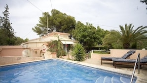 Una piscina con lettini e una casa sullo sfondo.
