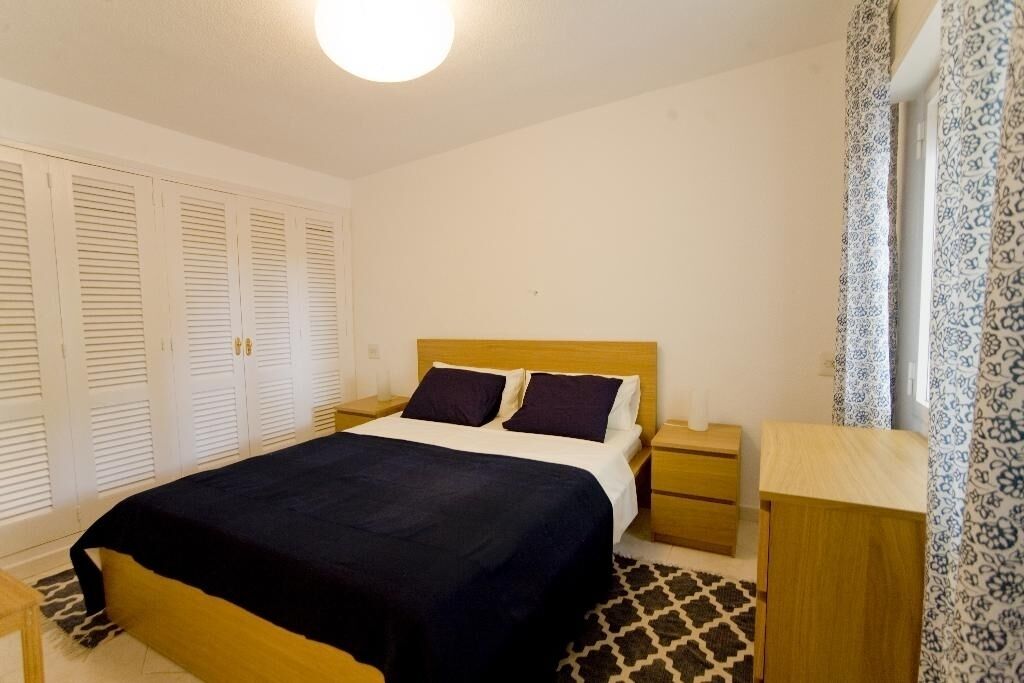 A bedroom with a bed, nightstands, a wooden dresser, and a patterned rug.