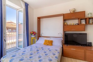 Une chambre à coucher comprenant un lit, une télévision, une armoire en bois et une fenêtre avec des rideaux.