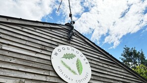 Een houten huisje met een bord waarop staat: WOODHOUSE HOLIDAY COTTAGE.