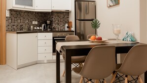 A modern kitchen with white cabinets, a black tiled backsplash, and stainless steel appliances. There is a dining table with chairs and a small plant on the table. - Monastiraki Urban Apartments (Athens)