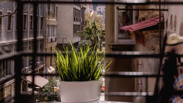 A balcony with a potted plant, a tiled table, and a view of buildings and a mountain in the background. - Monastiraki Urban Apartments (Athens)