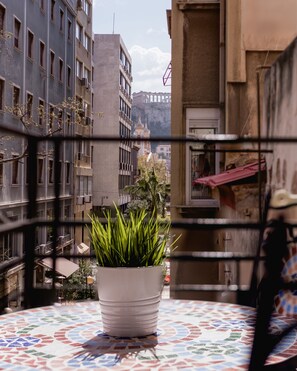 A balcony with a potted plant, a tiled table, and a view of buildings and a mountain in the background. - Monastiraki Urban Apartments (Athens)