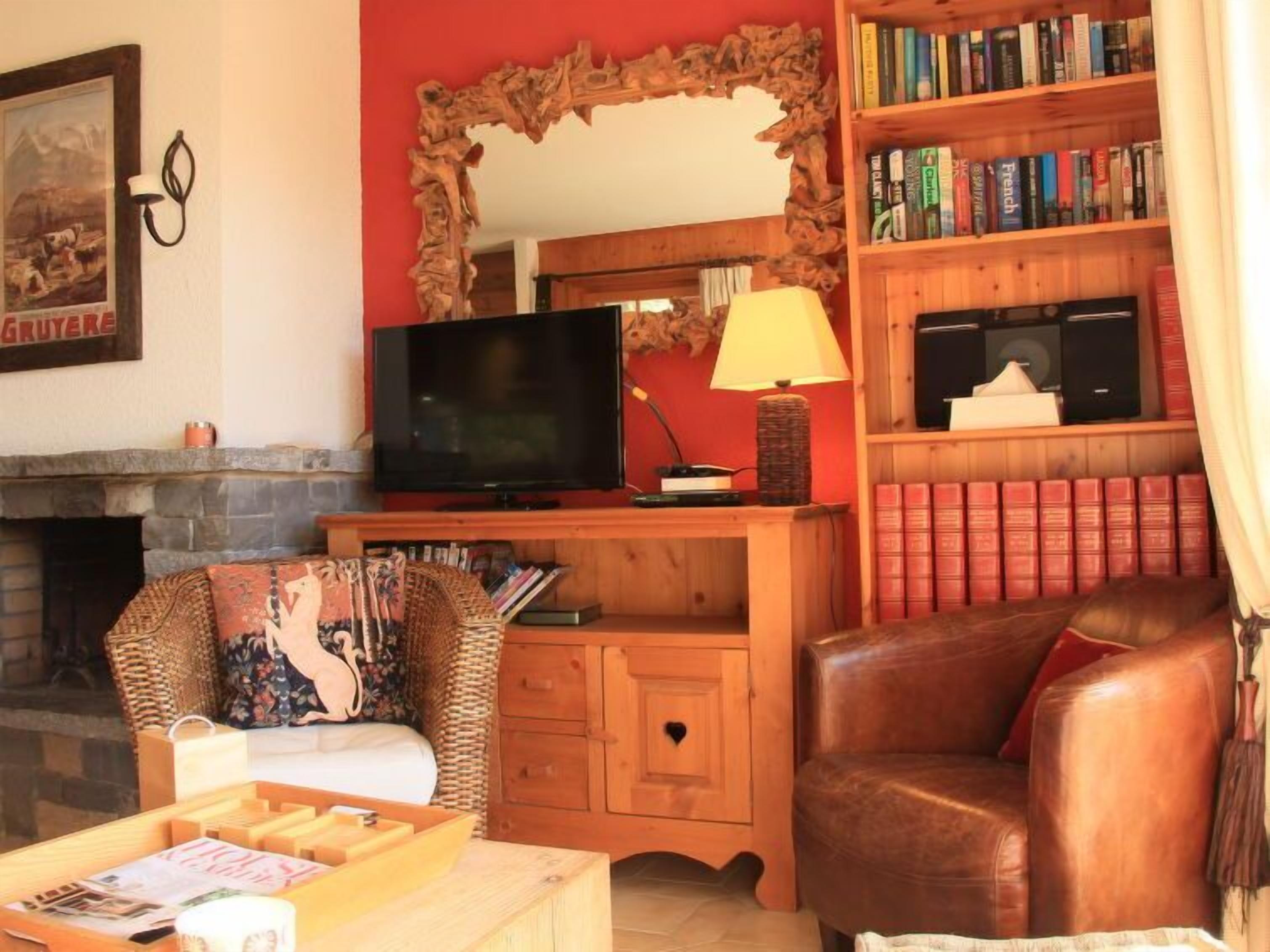 A cozy living room with a fireplace, a television, a bookshelf, and a leather armchair.