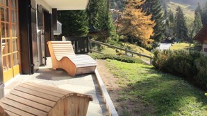 A wooden deck with a lounge chair, a stone pathway, and a view of a forested valley. - Armorial II / apt 2 by Interhome (Villars)