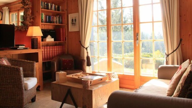 A cozy living room with a large window, a bookshelf, a television, and a comfortable seating area. - Armorial II / apt 2 by Interhome (Villars)