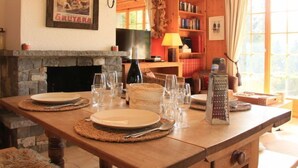 A dining area with a stone fireplace, a wooden table set for four, and a bookshelf in the background. - Armorial II / apt 2 by Interhome (Villars)