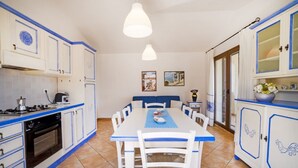Une cuisine avec des armoires blanches et des moulures bleues, une table à manger avec des chaises et un luminaire suspendu.