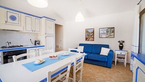 Une cuisine compacte avec des meubles blancs et des touches de bleu, une table à manger avec des chaises, et un canapé bleu dans l’espace salon.