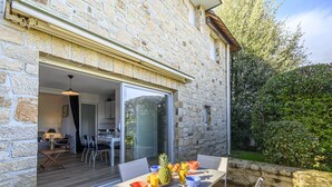 A stone building with a patio area featuring a table with chairs, a dining area, and a view of the surrounding greenery. - Océania II by Interhome (Carnac)