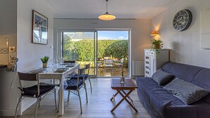 A modern living space with a dining area, a sofa, and a view of a garden through a sliding door. - Océania II by Interhome (Carnac)