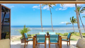 Varanda com mesa e cadeiras, vista para uma praia com palmeiras e o oceano.