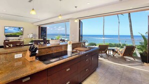Uma cozinha moderna com uma ilha grande, uma área de jantar com vista para o oceano e uma TV fixada na parede.