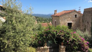 Un bâtiment en pierre, surmonté d’un toit en tuiles, entouré de verdure et offrant une vue sur des montagnes lointaines.