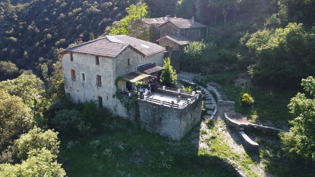 A stone building with a flat roof, surrounded by greenery and a stone pathway.