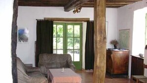 A rustic room with wooden beams, a green door, a sofa, a table, and a wooden cabinet.