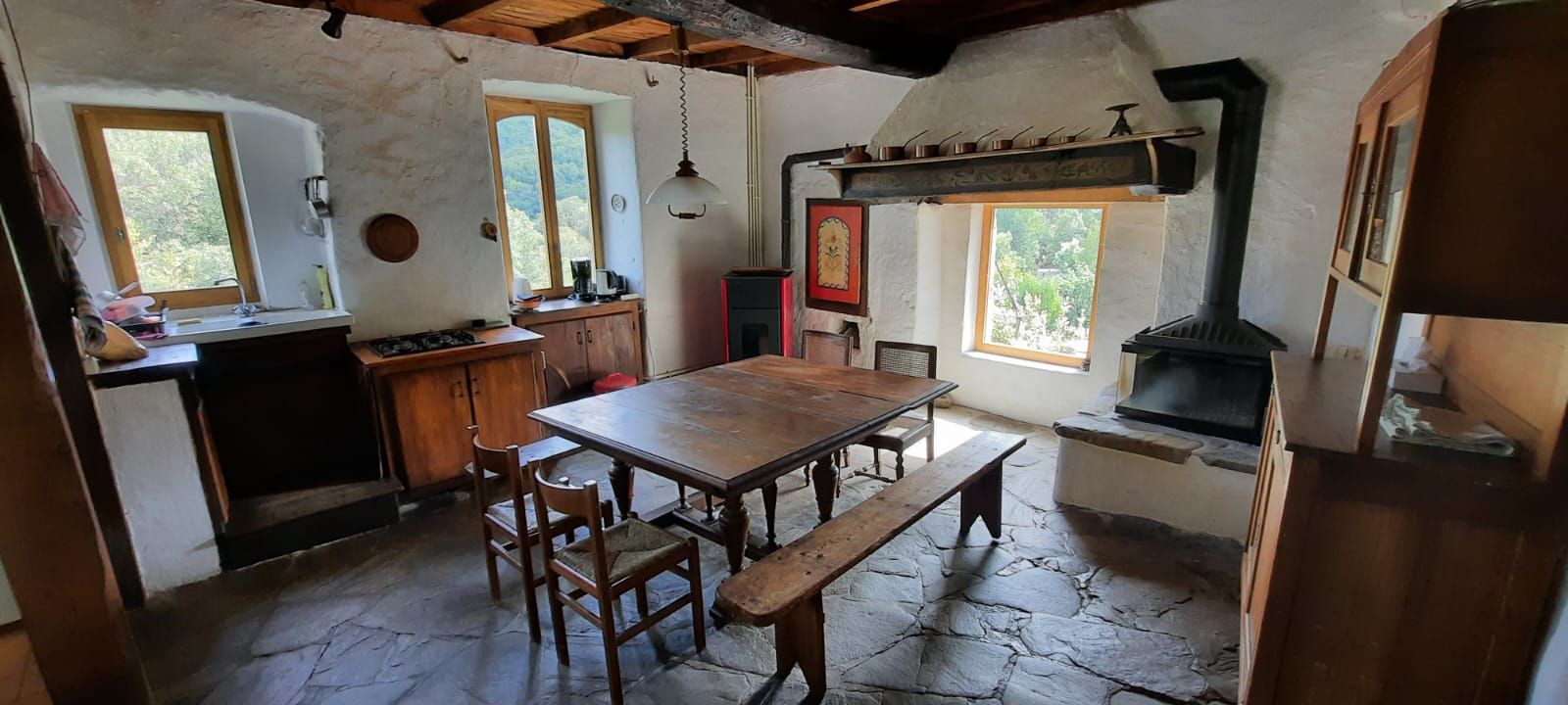 Una cocina rústica con una mesa de madera, suelo de piedra y un horno de leña.