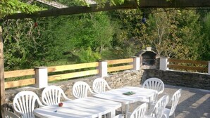 An outdoor patio with white plastic tables and chairs, surrounded by a stone wall and wooden fence, with a stone fireplace in the background.